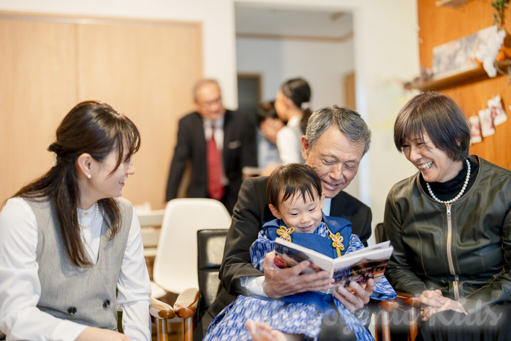 祖父母と一緒にお宮参りの写真集を見る家族の笑顔 千葉県鎌ケ谷市・道野辺八幡宮の出張撮影